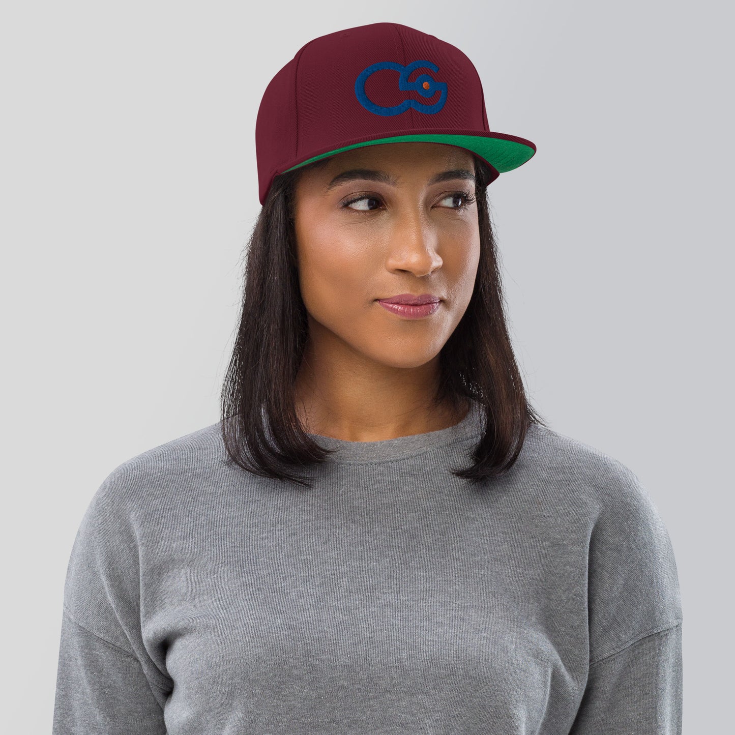 Crew Show logo snapback cap. Front view of woman wearing maroon colour snapback cap with the Crew Show logo embroidered on it.