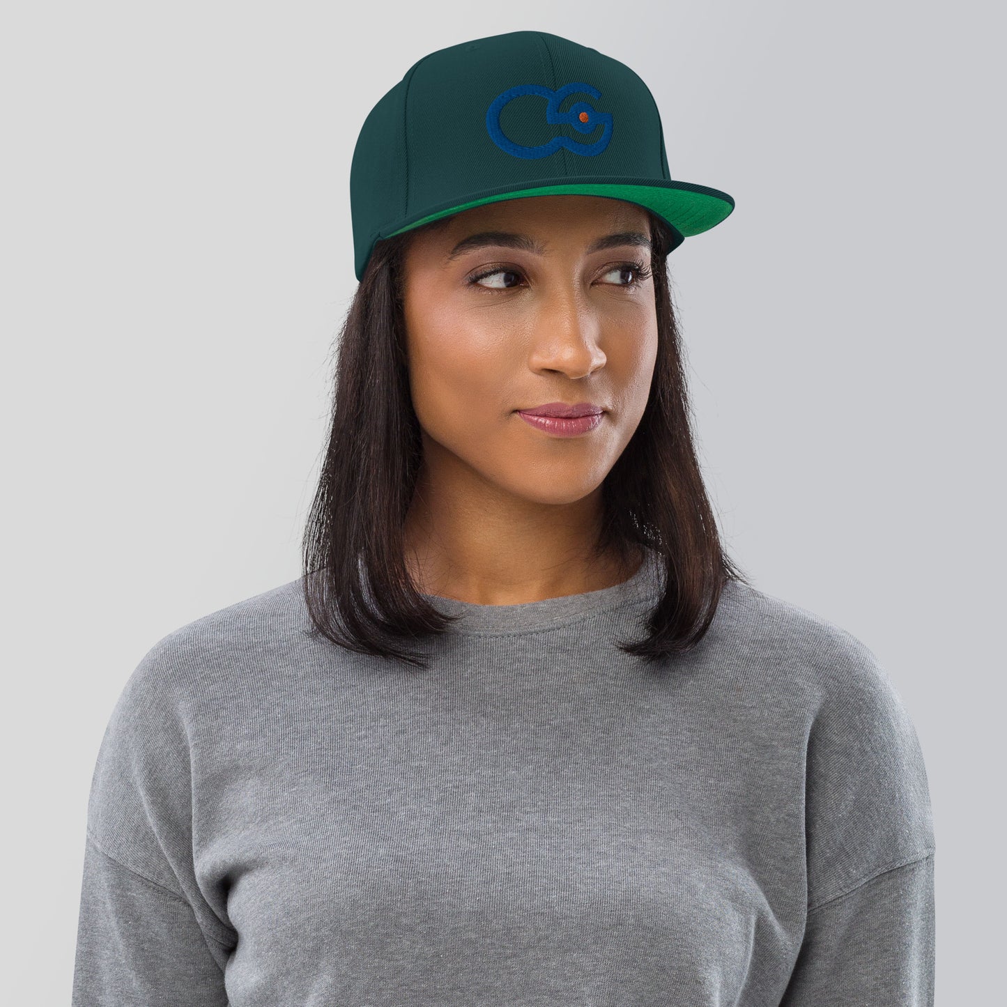 Crew Show logo snapback cap. Front view of woman wearing spruce green colour snapback cap with the Crew Show logo embroidered on it.